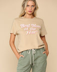 Model wearing sand colored tee with a bold retro style print with pink and white font that reads "best mom of the year"