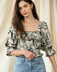 Model wears top with a fitted, smocked bodice, puff sleeve with elastic at ends, square neckline in a beautiful black and ivory floral print