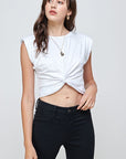 Model wearing the Gabi tank in white. Tank has a slightly scoop crew neckline, sleeves go to end of shoulder with slight padding for structure. Front has a twist creating an inverted V and adding to the cropped length of the tank. Paired with Black denim and simple jewlery.