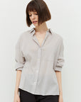 model with a brown bob wearing the Marta shirt, 3/4 buttoned with sleeves rolled up. Shows the straight hem and txtured weave of the lgihtweight material. Color is a very pale grey with undertones of purple.