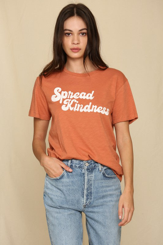 model wearing retro font tee that reads &quot;sprad kindness&quot; in a muted red-orange color.