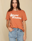 model wearing retro font tee that reads "sprad kindness" in a muted red-orange color.