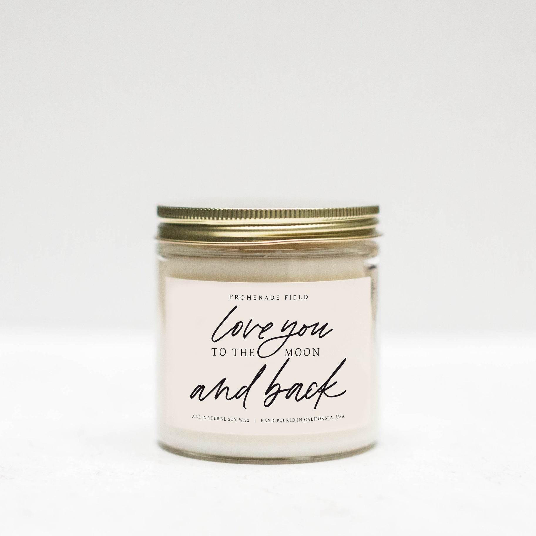 Jar candle with gold lid, white label which says "Love you to the moon and back" in cursive font.
