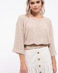 Blond Haired model wears the two tone top, shows wide sleeves, dropped shoulder, round neckline and smocked bottom hem giving the shirt more volume. Paired with an off white button front skirt.