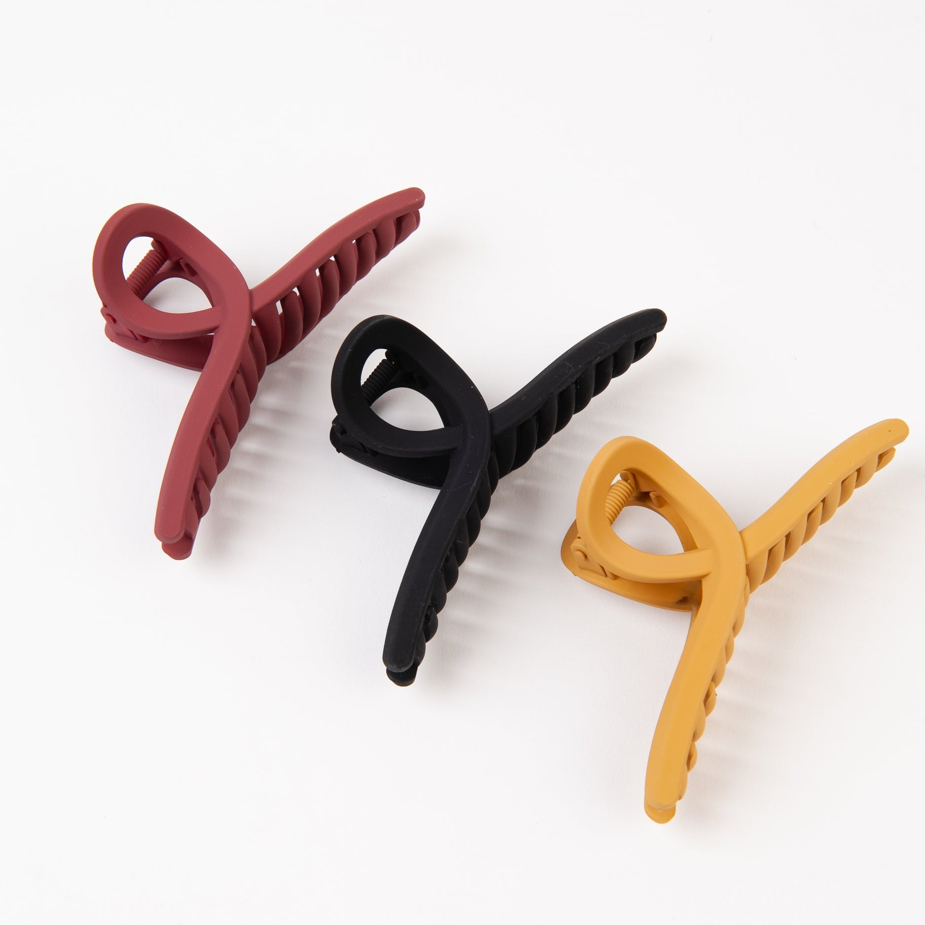 Hair Claw clip, with wide bottom and twisted loop top. Shown in three colors: Merlot/Rust, Black and Mustard Yellow.