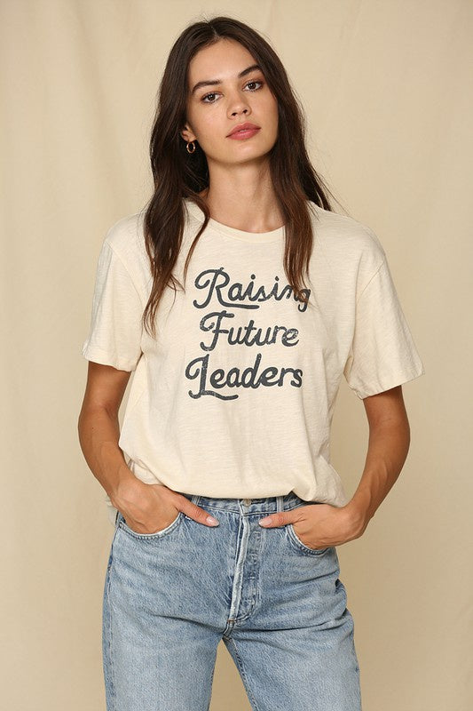 Model wearing bone colored shirt with retro dark gray font that reads &quot;Raising Future Leaders&quot; 