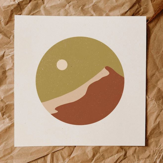 Minimalist print has no defined lines, features a mustard color speckled sky with cream color moon to the left, warm brown mountain with a peach side. Design is a circle shape with white background.