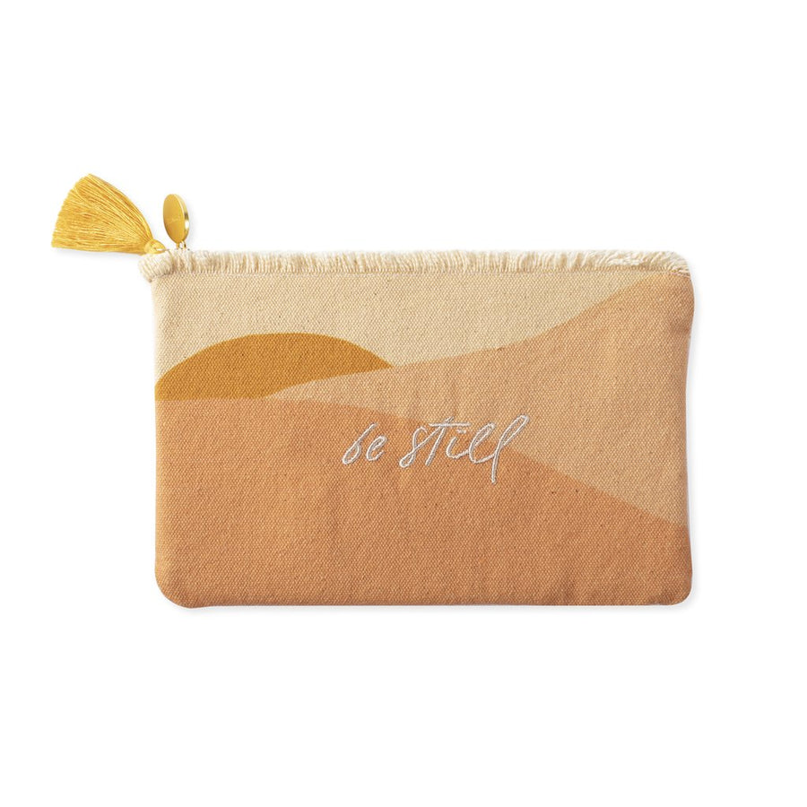 cloth pouch with shades of yellow and orange abstract design, white embroidery says "be still". Zipper pull has gold tassel.