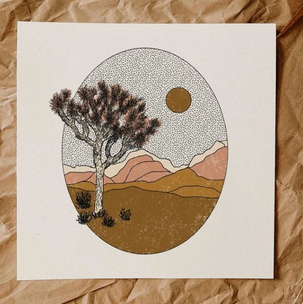 Art print featuring an oval shape with a Joshua Tree and shrubs in the front and mountains in tan and terracotta shades in the back. Sky has hashmark design and godl sun.
